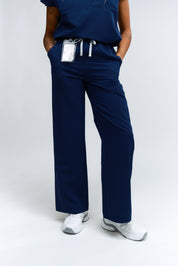 A person wearing navy wide leg scrub pants with an elastic waistband, standing against a white background.