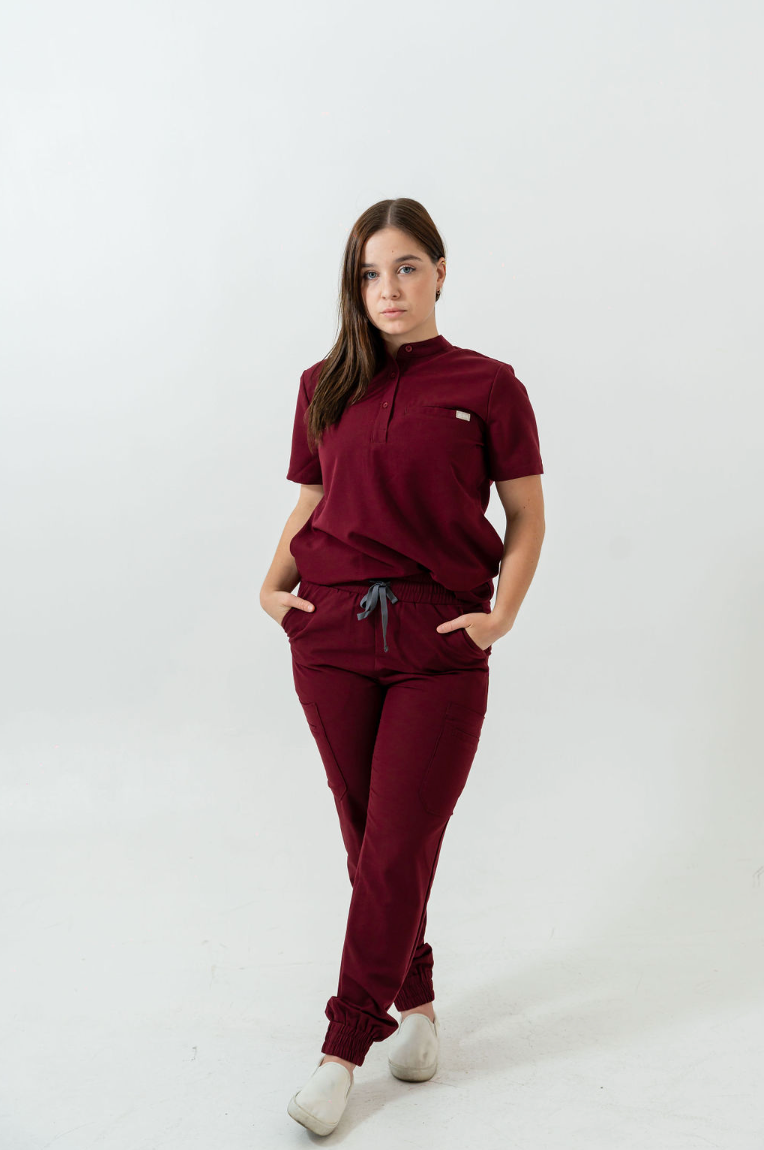 A person standing wearing burgundy scrub pants with multiple pockets and a drawstring waist.