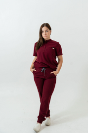 A person standing wearing burgundy scrub pants with multiple pockets and a drawstring waist.