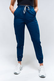 A person standing wearing blue jogger scrub pants with a drawstring waistband, paired with white sneakers.