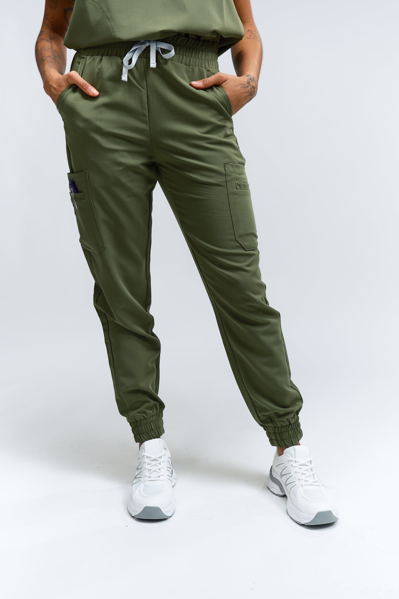 A person wearing mossy green scrub pants with multiple pockets and a drawstring waist, paired with white sneakers.